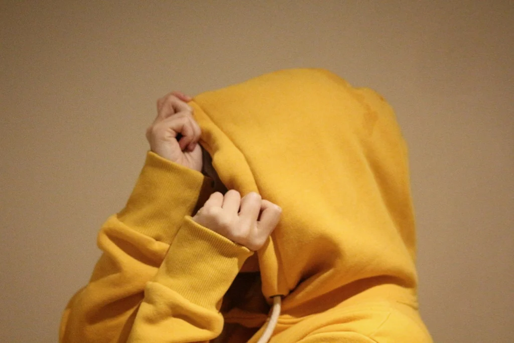 Pessoa de moletom amarelo escondendo o rosto com o capuz